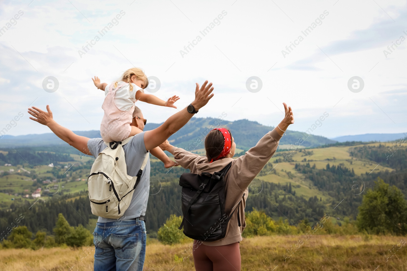 Photo of Family of tourists with backpacks enjoying picturesque landscape with wide open arms, back view. Space for text