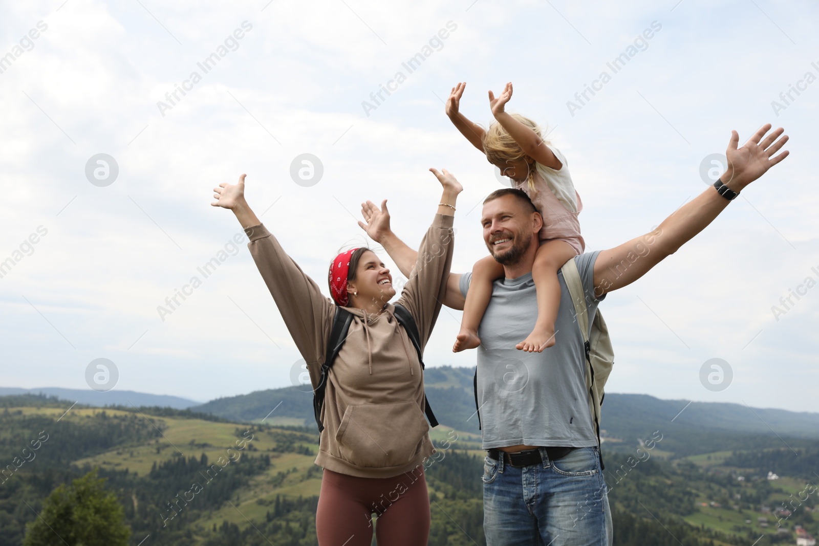 Photo of Happy tourists with backpacks enjoying picturesque landscape with wide open arms