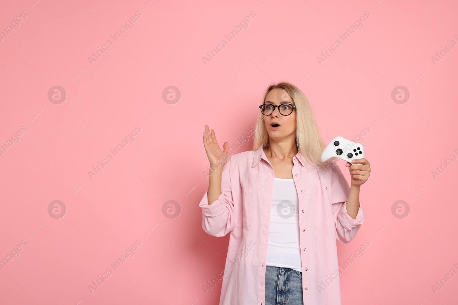 Photo of Surprised woman with controller on pink background, space for text