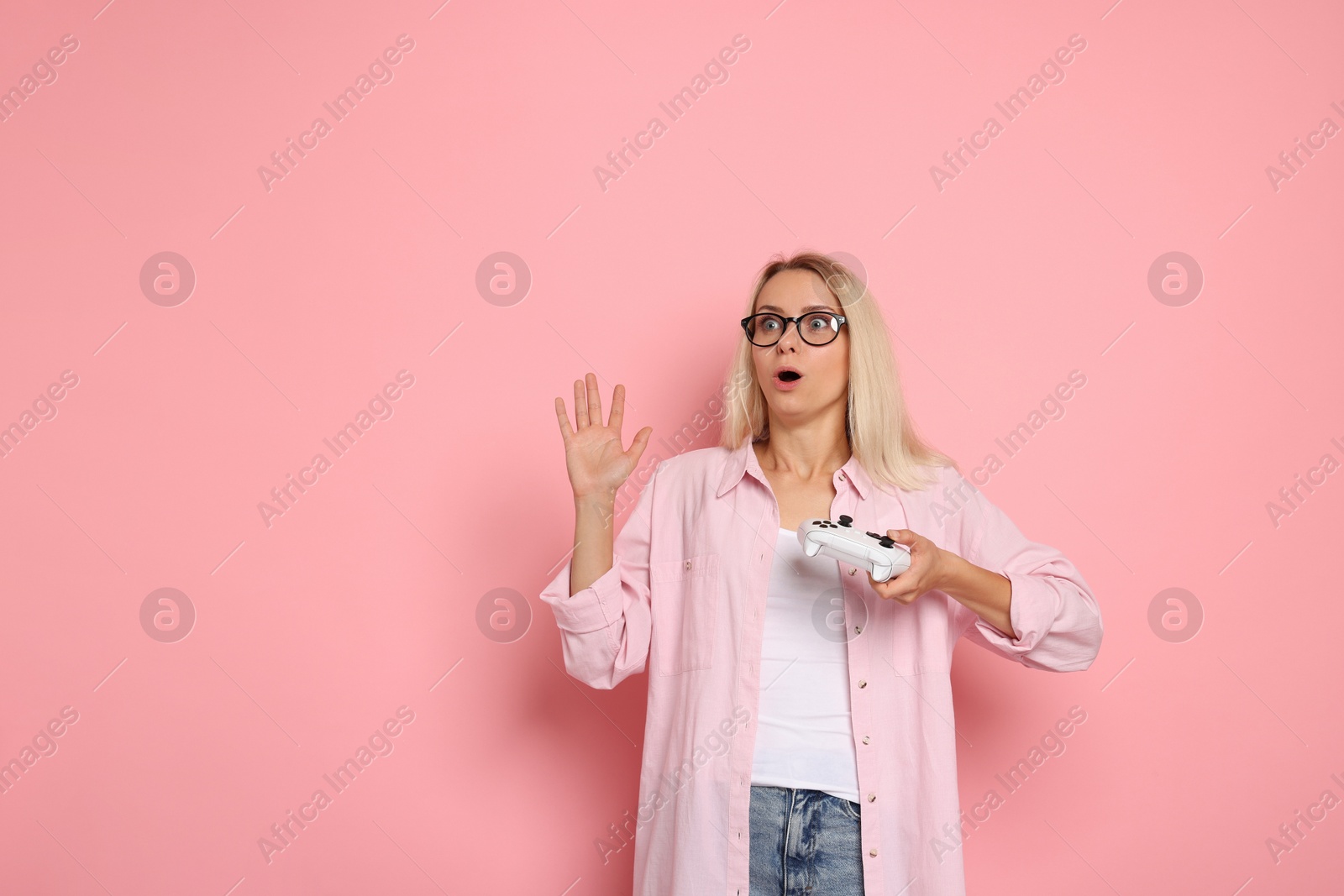 Photo of Surprised woman with controller on pink background, space for text