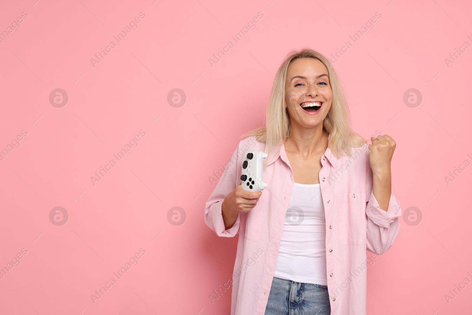 Photo of Happy woman with controller on pink background, space for text