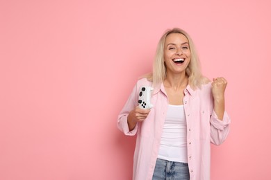 Happy woman with controller on pink background, space for text