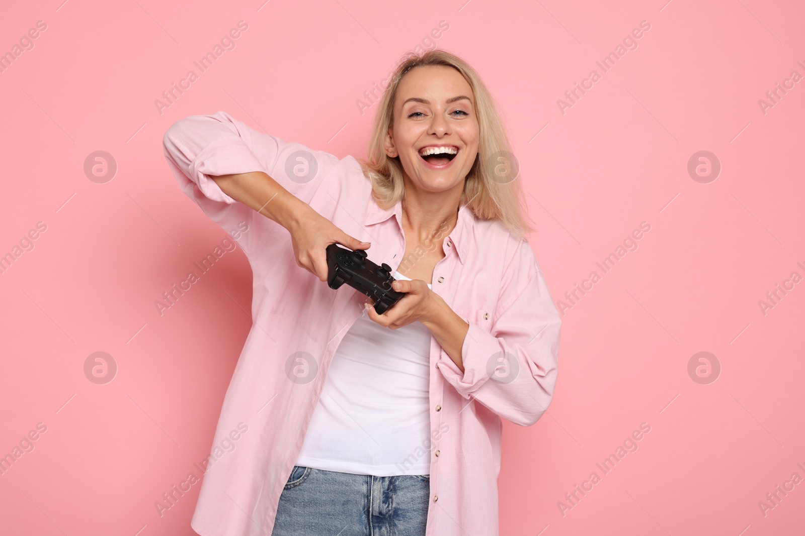 Photo of Happy woman playing video games with controller on pink background