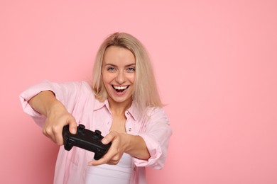 Happy woman playing video games with controller on pink background, space for text