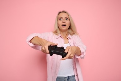 Excited woman playing video games with controller on pink background