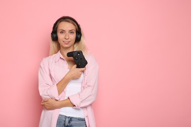 Happy woman in headphones with controller on pink background, space for text