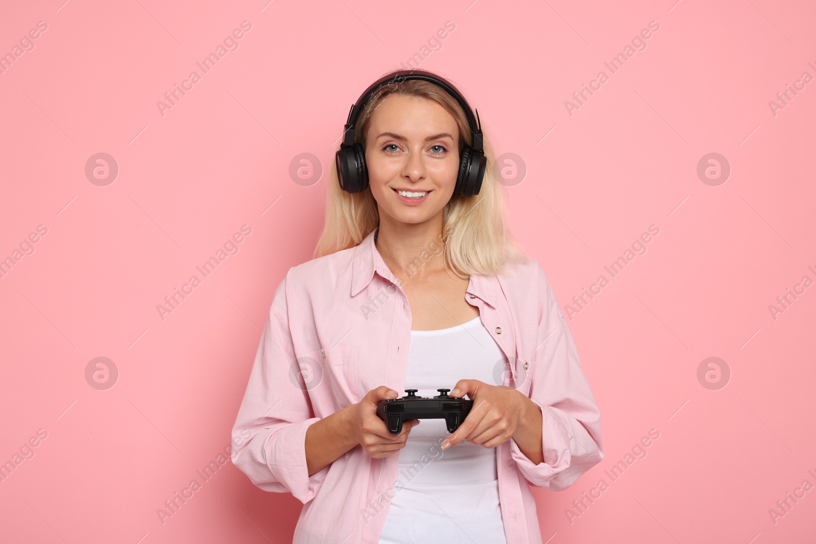 Photo of Happy woman in headphones playing video games with controller on pink background