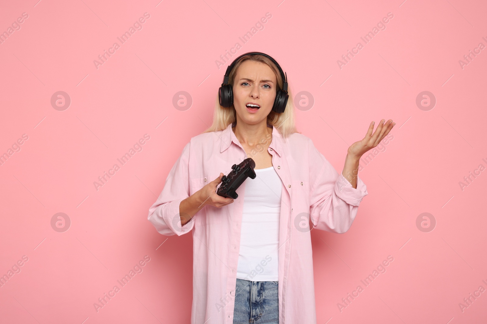 Photo of Unhappy woman in headphones playing video games with controller on pink background