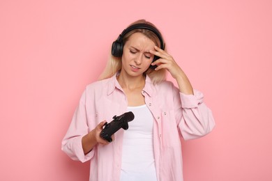 Photo of Unhappy woman in headphones playing video games with controller on pink background