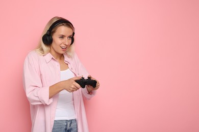 Woman in headphones playing video games with controller on pink background, space for text