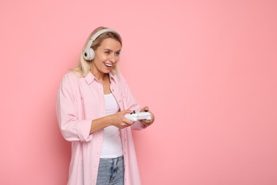 Happy woman in headphones playing video games with controller on pink background, space for text