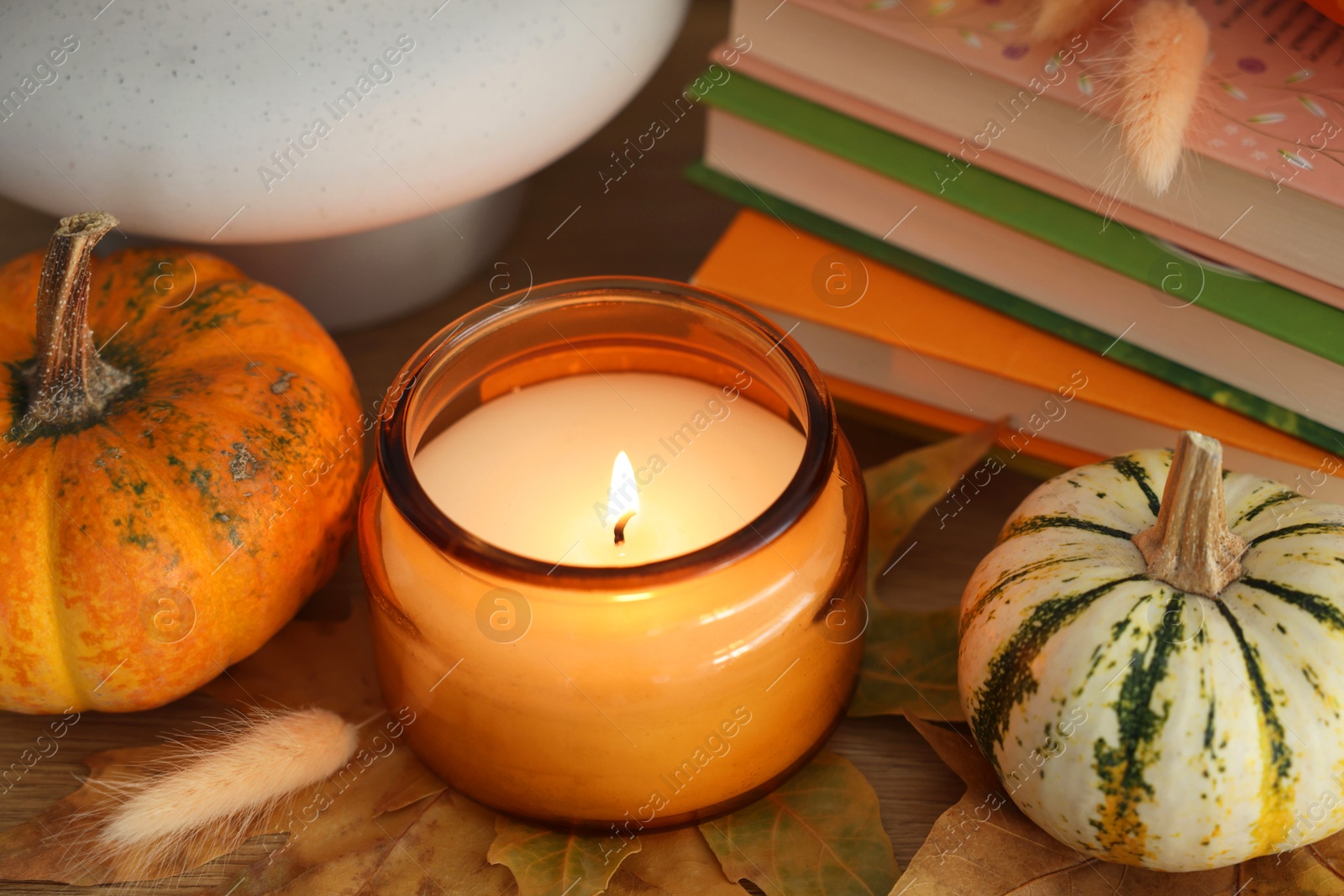 Photo of Burning candle, pumpkins and stack of books on wooden table, closeup. Autumn atmosphere