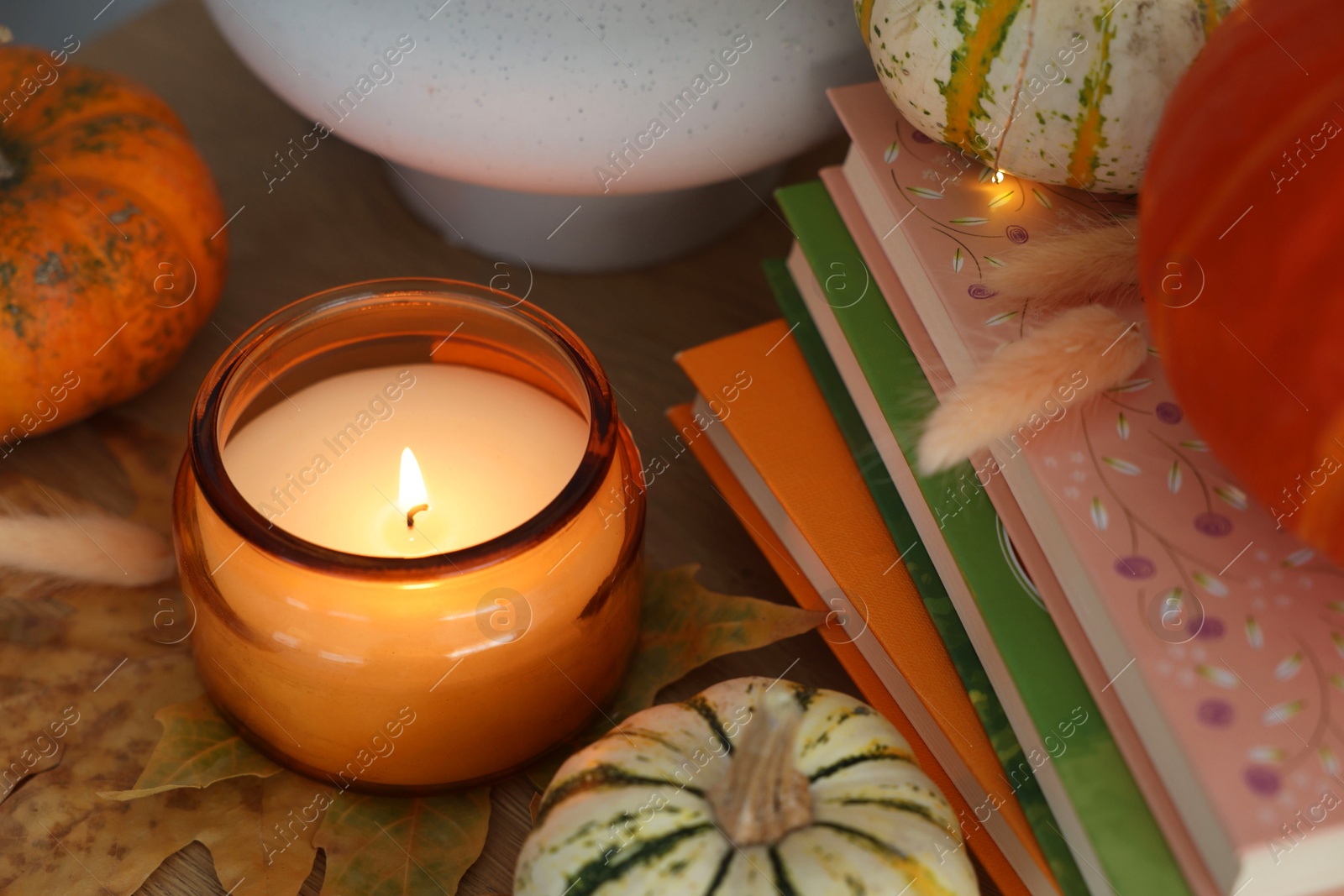 Photo of Burning candle, pumpkins and stack of books on wooden table, closeup. Autumn atmosphere