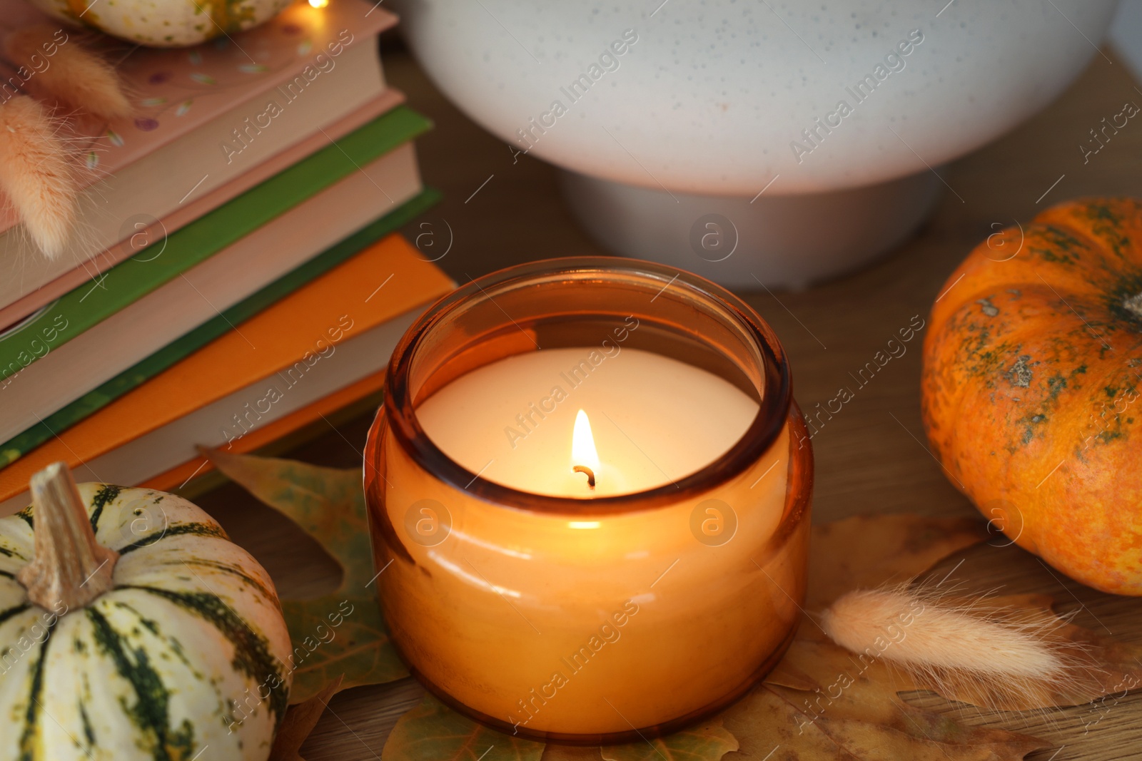 Photo of Burning candle, pumpkins and stack of books on wooden table, closeup. Autumn atmosphere