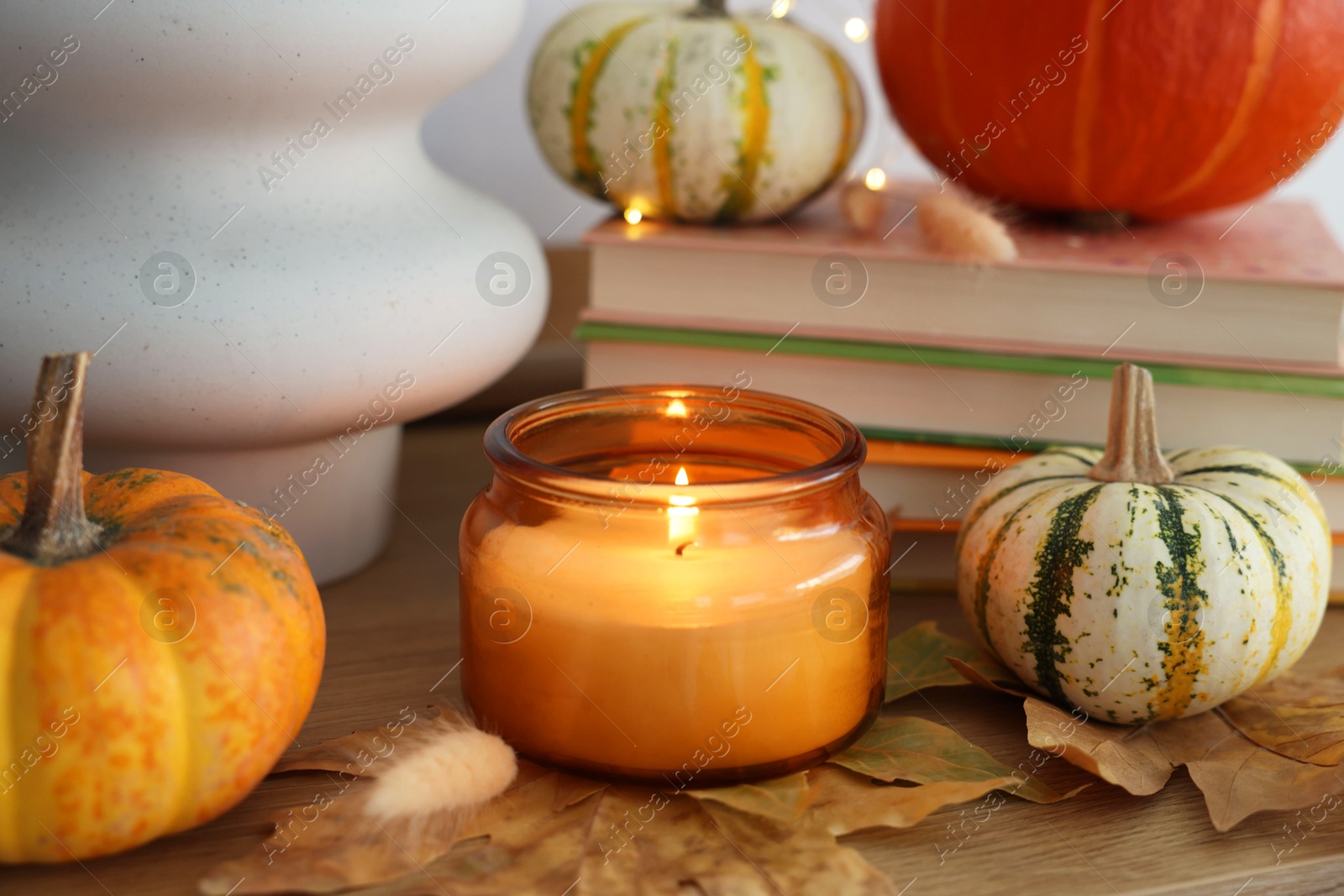 Photo of Burning candle, pumpkins and dry leaves on wooden table, closeup. Autumn atmosphere