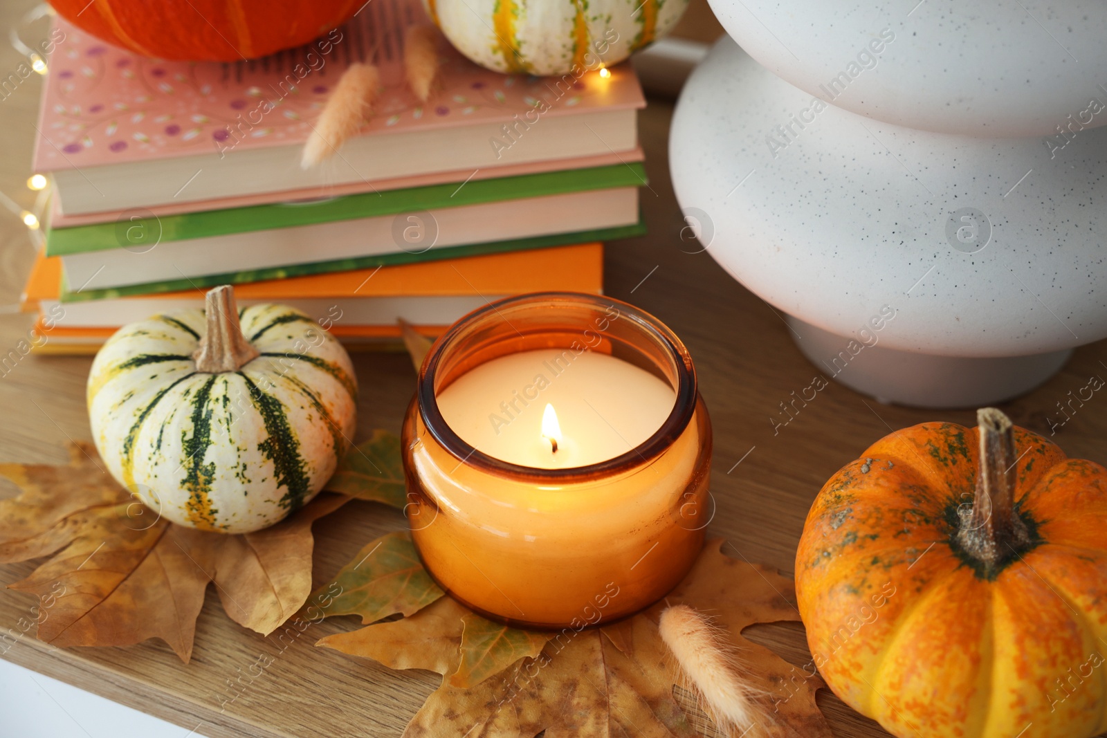 Photo of Burning candle, pumpkins and stack of books on wooden table, closeup. Autumn atmosphere