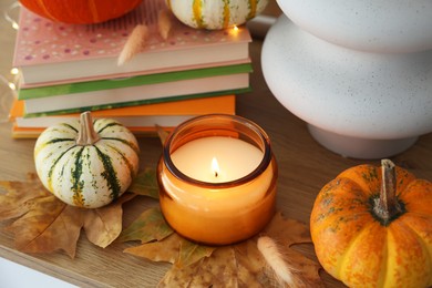 Photo of Burning candle, pumpkins and stack of books on wooden table, closeup. Autumn atmosphere