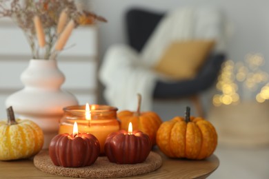 Photo of Burning candles and pumpkins on wooden table indoors, space for text. Autumn atmosphere