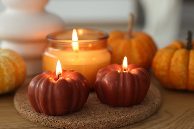 Photo of Burning candles and pumpkins on wooden table, closeup. Autumn atmosphere