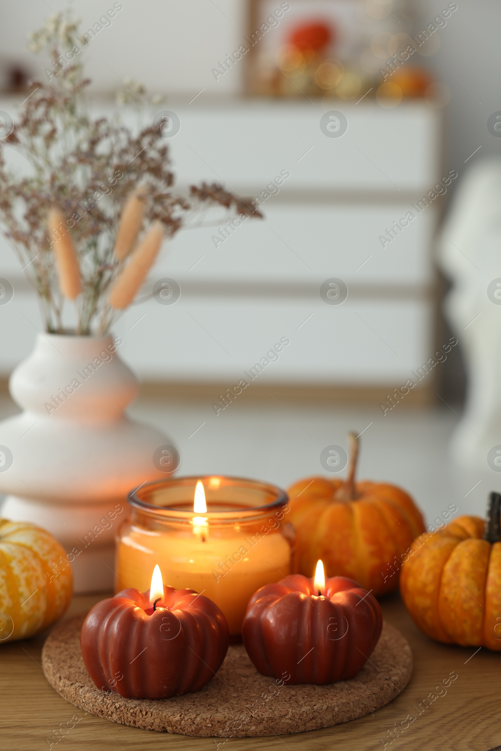 Photo of Burning candles and pumpkins on wooden table indoors, space for text. Autumn atmosphere