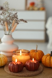 Photo of Burning candles and pumpkins on wooden table indoors, space for text. Autumn atmosphere