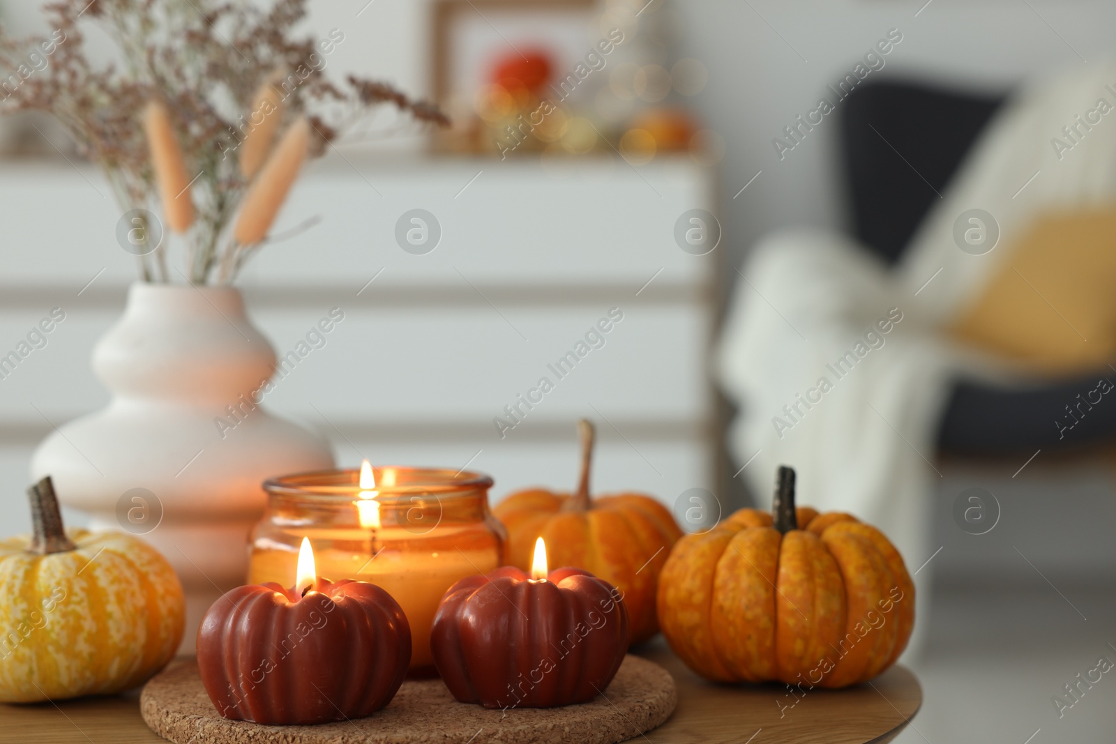 Photo of Burning candles and pumpkins on wooden table indoors, space for text. Autumn atmosphere