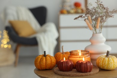 Photo of Burning candles and pumpkins on wooden table indoors, space for text. Autumn atmosphere