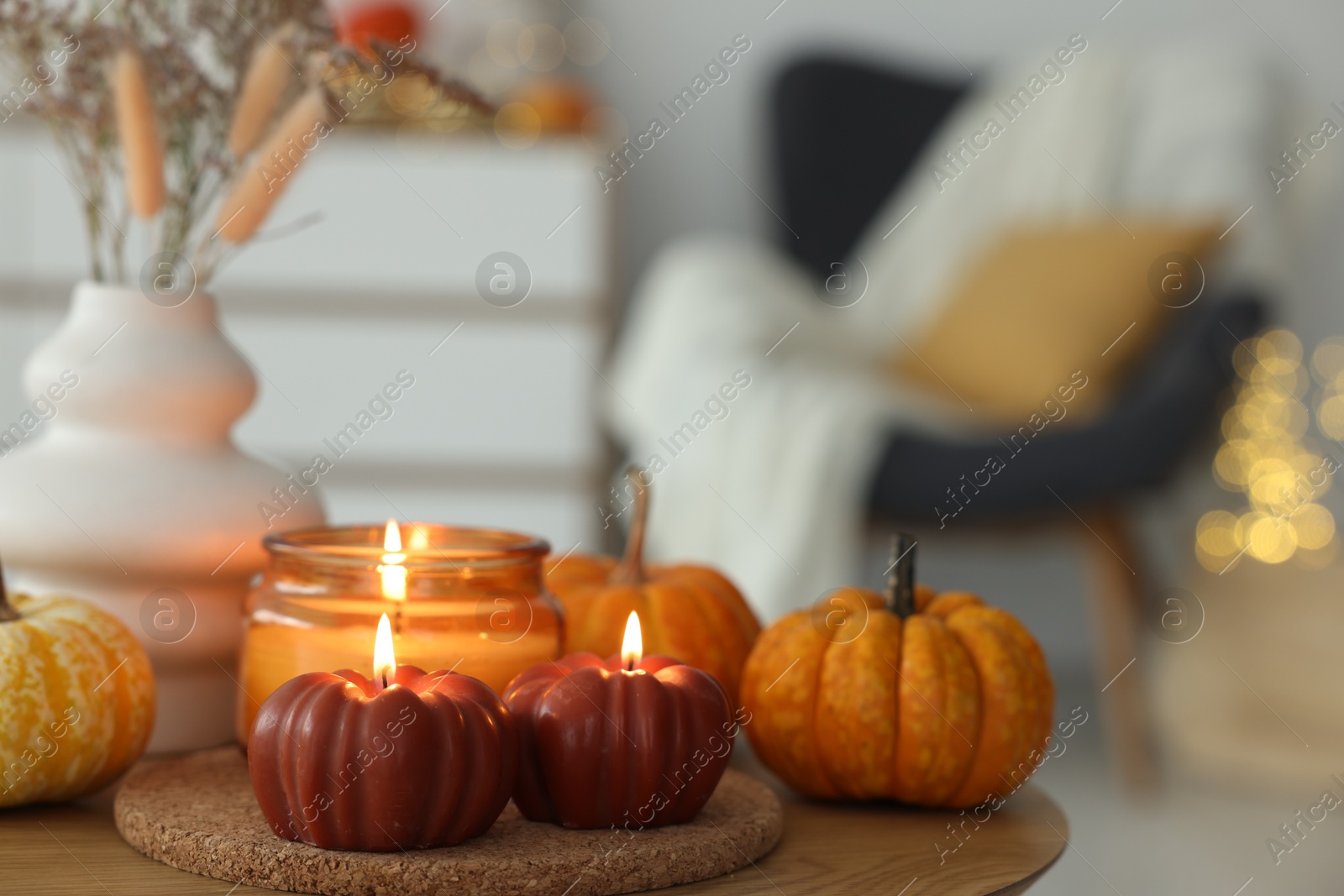 Photo of Burning candles and pumpkins on wooden table indoors, space for text. Autumn atmosphere