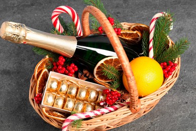 Wicker gift basket with sparkling wine and Christmas decor on grey textured table