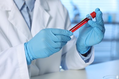 Photo of Laboratory testing. Doctor holding test tube with blood sample at table indoors, closeup