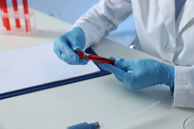 Laboratory testing. Doctor holding test tube with blood sample at table indoors, closeup