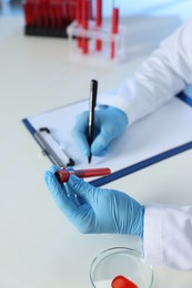 Photo of Laboratory testing. Doctor with blood sample taking notes at table indoors, closeup