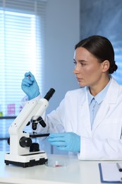 Photo of Laboratory testing. Doctor holding pipette and working with microscope at table indoors