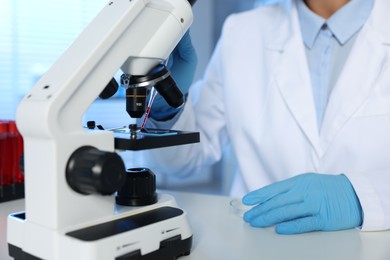 Laboratory testing. Doctor dripping blood sample onto glass slide while working with microscope at table indoors, closeup