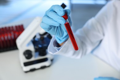 Photo of Laboratory testing. Doctor holding test tube with blood sample at table indoors, closeup