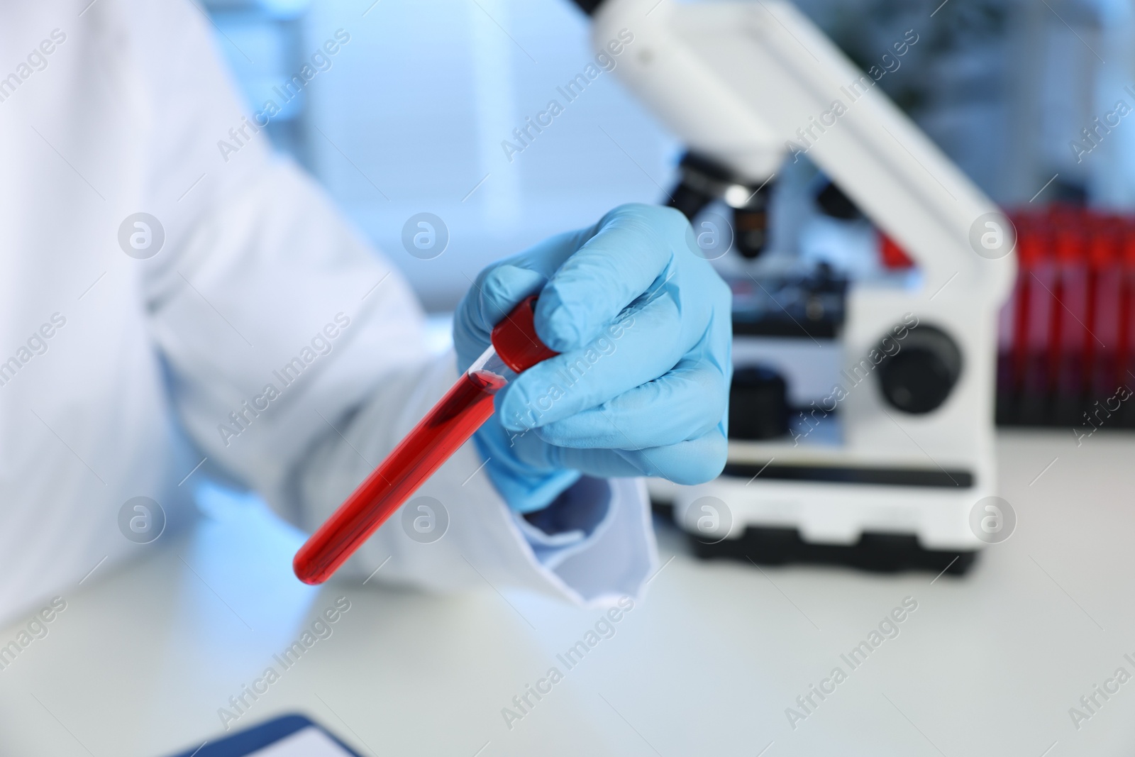 Photo of Laboratory testing. Doctor holding test tube with blood sample at table indoors, closeup