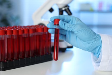 Laboratory testing. Doctor holding test tube with blood sample at table indoors, closeup