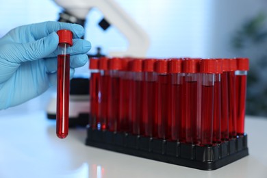 Laboratory testing. Doctor holding test tube with blood sample at table indoors, closeup