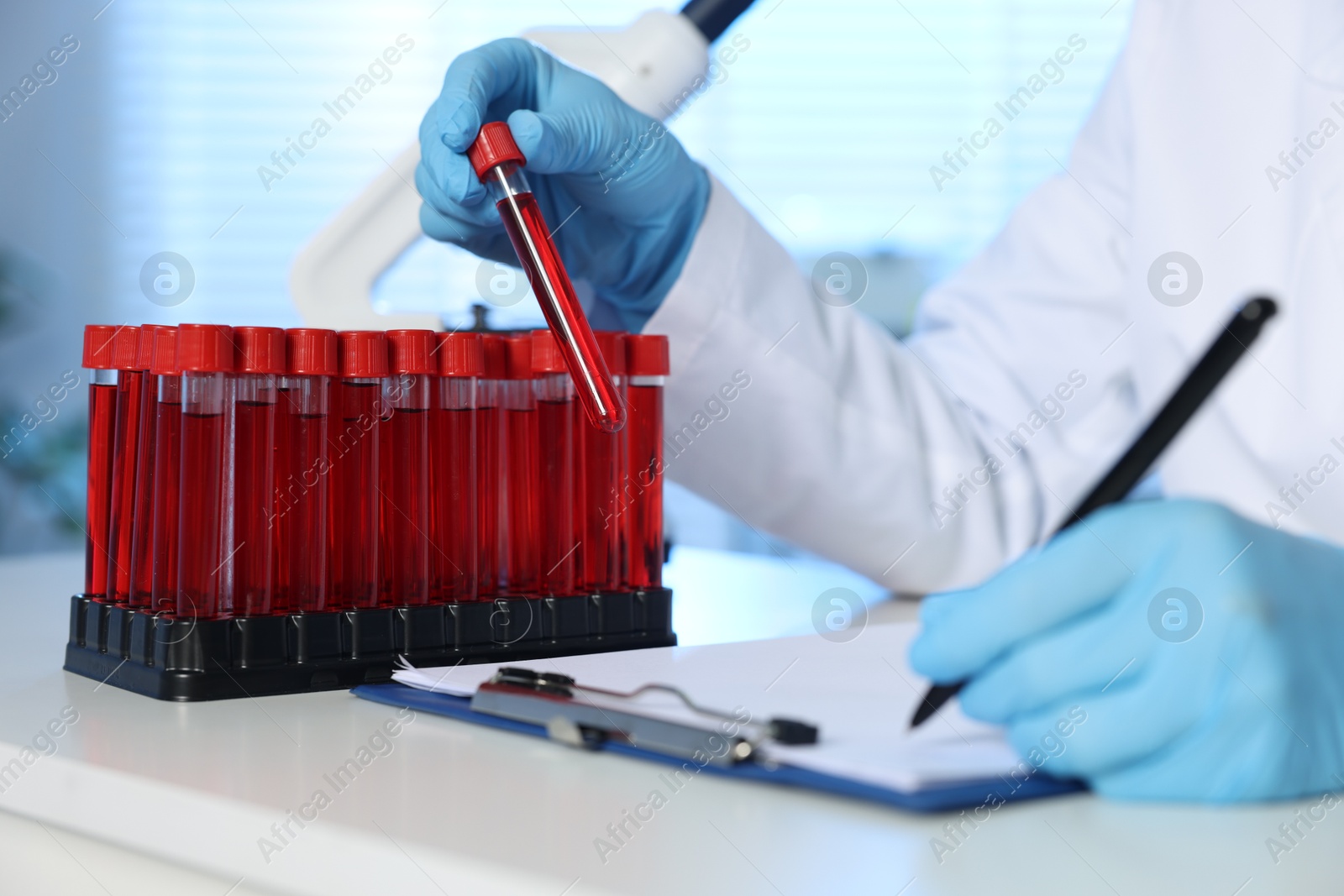 Photo of Laboratory testing. Doctor taking test tube with blood sample while working at table indoors, closeup