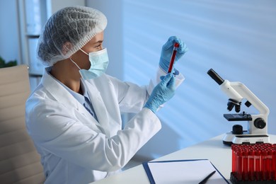 Laboratory testing. Doctor holding test tube with blood sample at table indoors