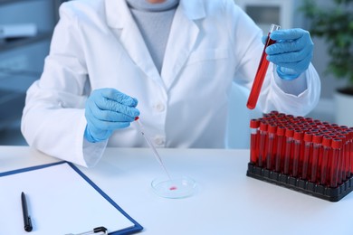 Photo of Laboratory testing. Doctor with test tube dripping blood sample into Petri dish at table indoors, closeup