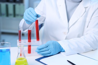 Photo of Laboratory testing. Doctor taking test tube with blood sample at table indoors, closeup