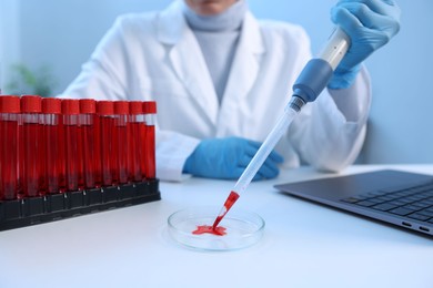 Photo of Laboratory testing. Doctor dripping blood sample into Petri dish at table indoors, closeup