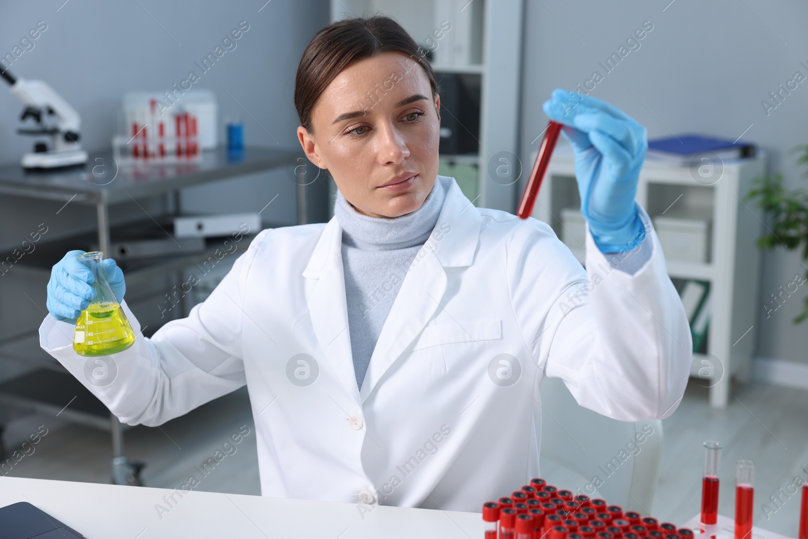 Photo of Laboratory testing. Doctor with blood sample in tube and flask at table indoors