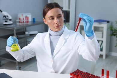 Photo of Laboratory testing. Doctor with blood sample in tube and flask at table indoors