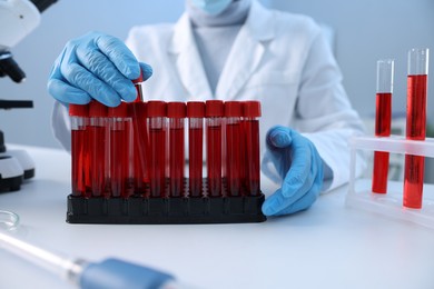 Laboratory testing. Doctor taking test tube with blood sample at table indoors, closeup