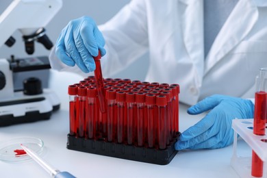 Laboratory testing. Doctor taking test tube with blood sample at table indoors, closeup