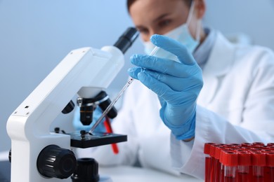 Laboratory testing. Doctor dripping blood sample onto glass slide while working with microscope indoors, selective focus