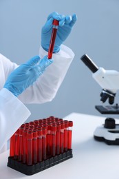 Laboratory testing. Doctor holding test tube with blood sample at table indoors, closeup