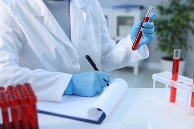 Laboratory testing. Doctor with blood sample taking notes at table indoors, closeup